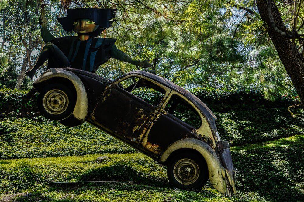 old yellow volkswagon hung from a tree; character sitting a top it