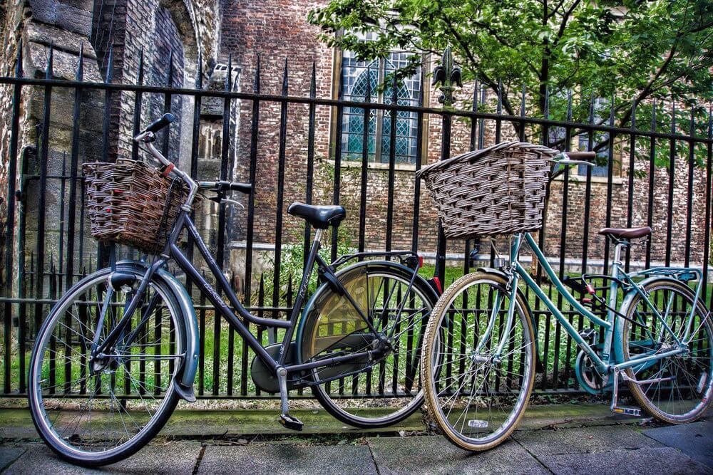 2 biciclyes leaning up against a rod iron fence in Cambridge