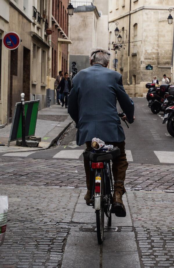 Back of man riding bike with a baguette on the back of the bike