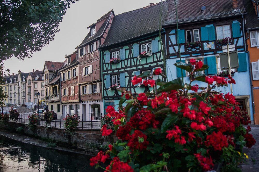 Visit Colmar France: Red geraniums, blue half timbered house and the canal