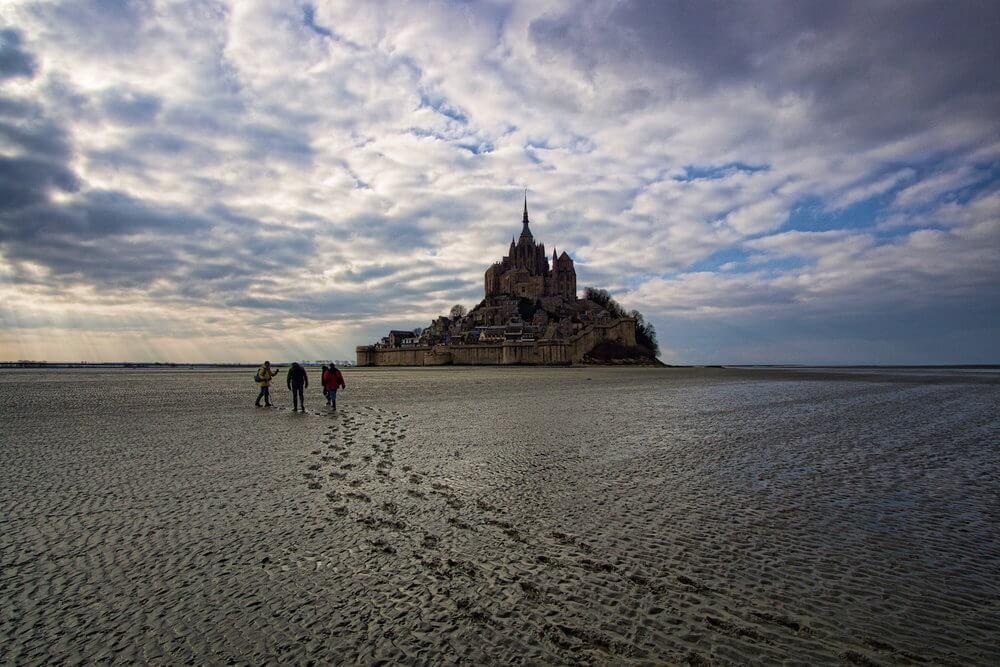 Visiting le Mont Saint Michel  3 people walking on the baie with the church soaring