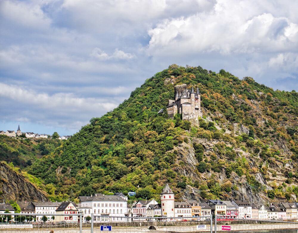 Rhine river: town along the river; a stone castle with pointed turrets in the hill above
