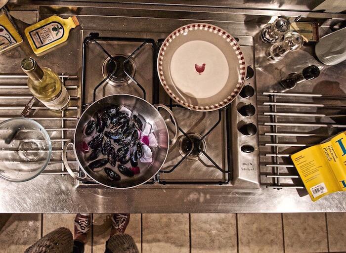 Top down view of the stove with a pot of mussels , wine and an empty bowl, cooks feet below