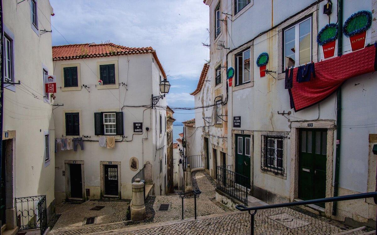 white washed buildings_hanging red sheet_cobbled laneway_ one day in Lisbon