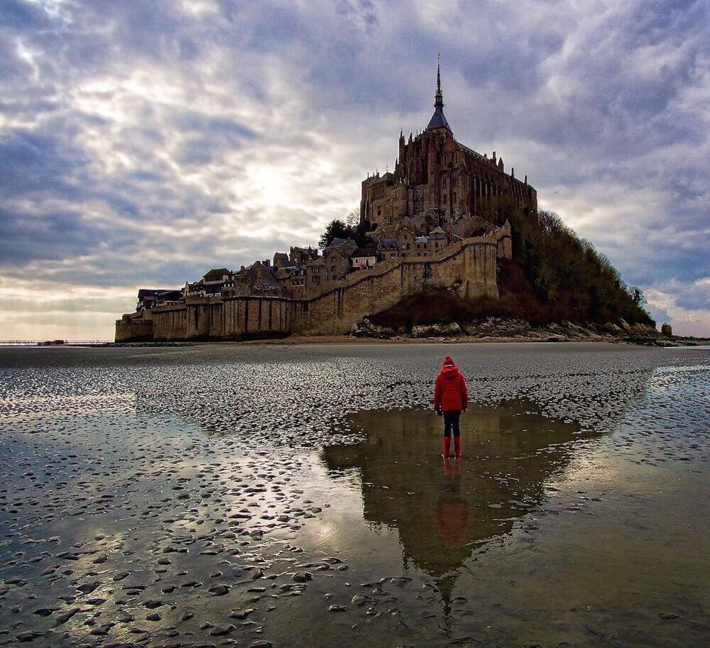 Mont saint michel and a child with a reflection standing on the sand at low tide