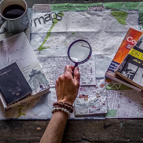 plan my journey: maps, travel books stacked. hand holding magnifying glass