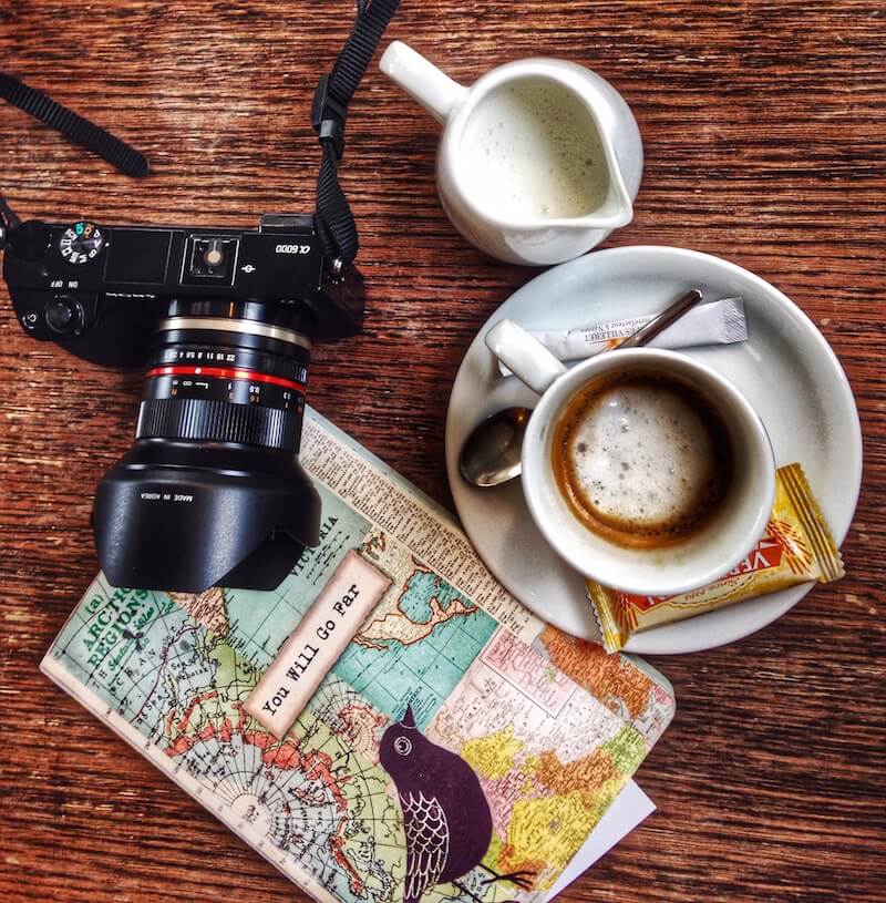 top down view - camera, coffee and travel journal on the cover "You Will Go Far"