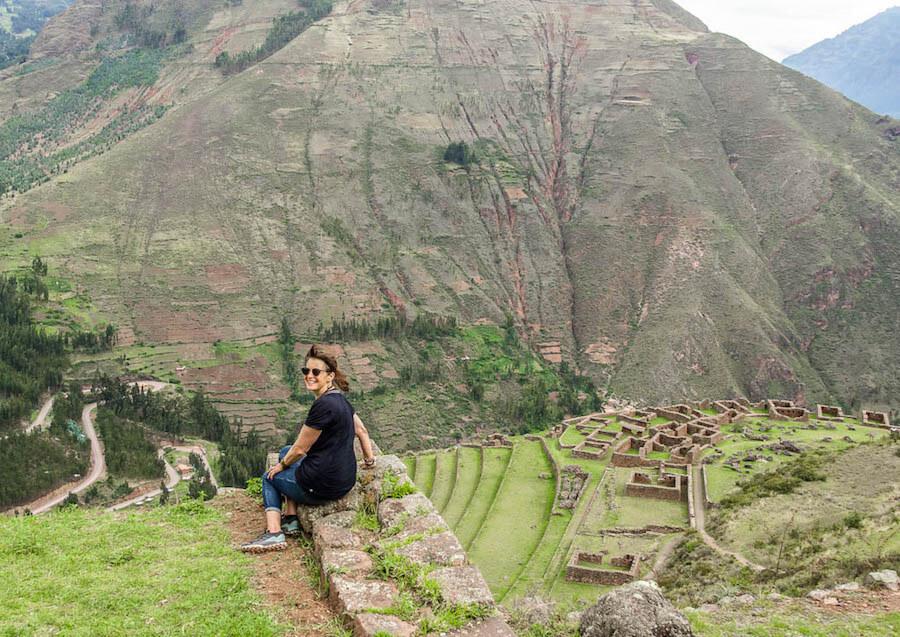 solo travel over 50: lady sitting and looking over shoulder at camera; Andes in the back and view over the ruins