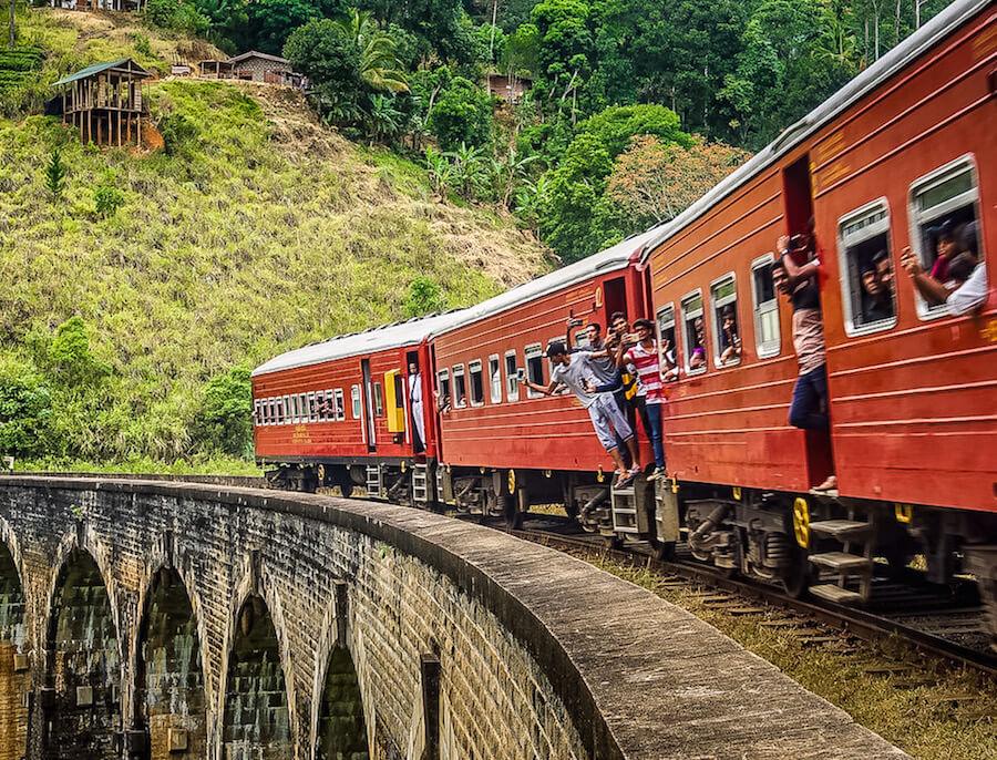 Welcome to Sri Lanka - red train crossing 9 arch bridge, people hanging out of the train doors and windows