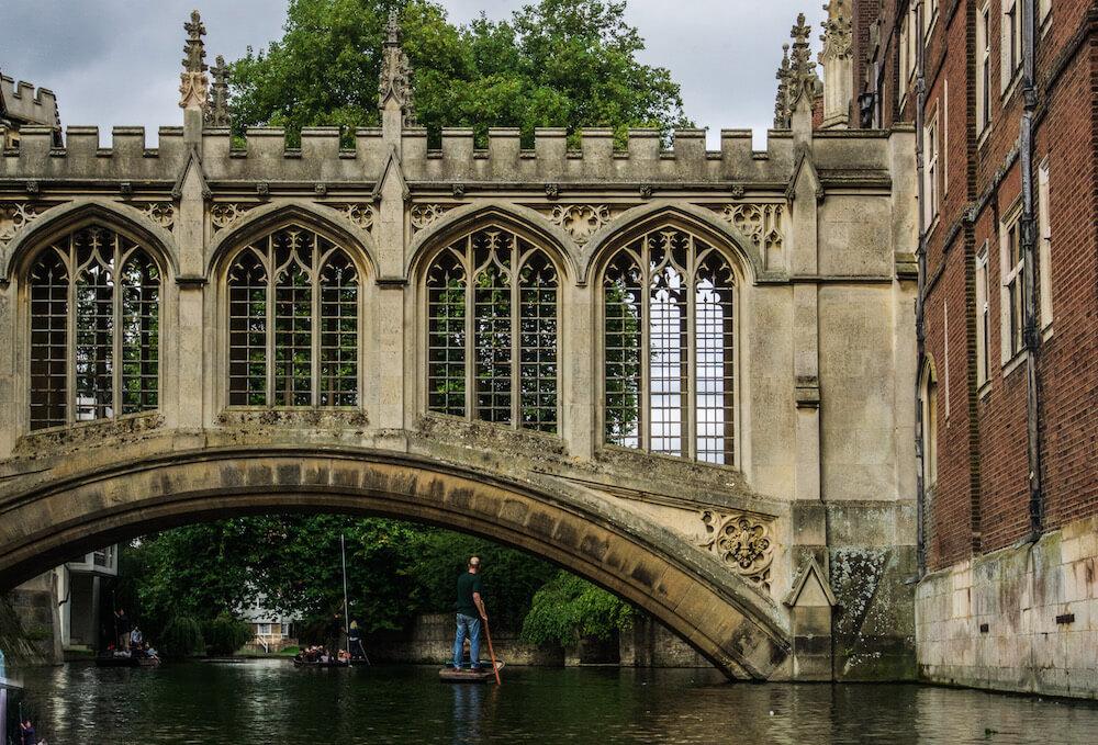 Welcome to England| The arched bridge of sighs over the River Cam and a punted standing and punting under the bridge