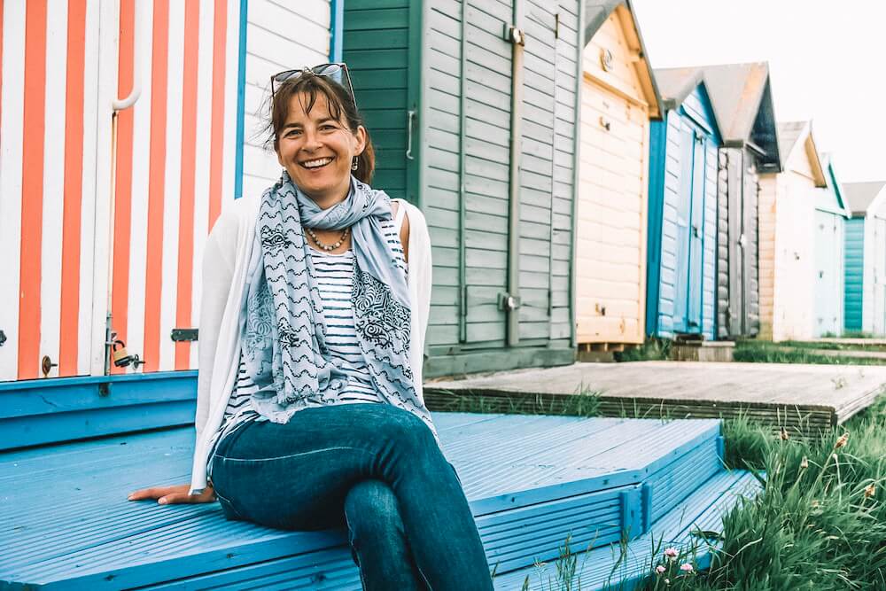 Follow your dreams beyond the comfort zone. Alison Browne sitting in front of striped beach huts 