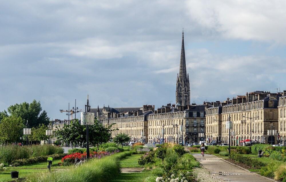 Walkway with beautiful buildings behind them is a soaring spire, be sure to Visit Bordeaux 