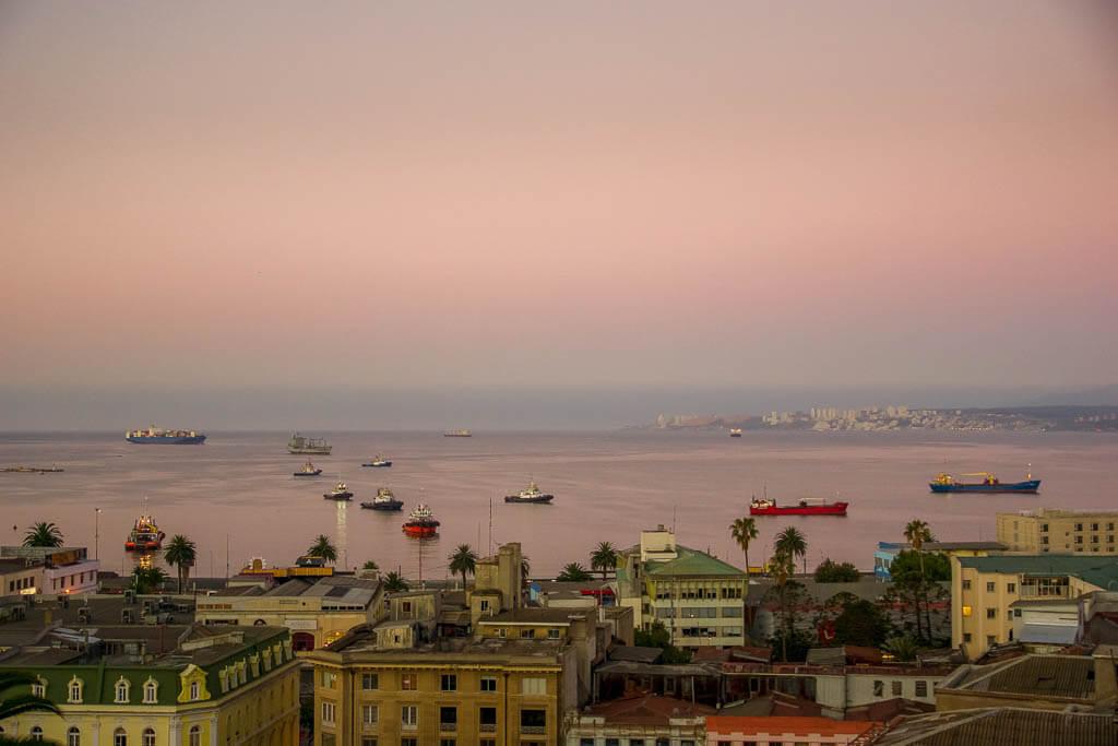 Visit Chile: gorgeous pink sky over the ocean with boats afloat and golden buildings in the forefront