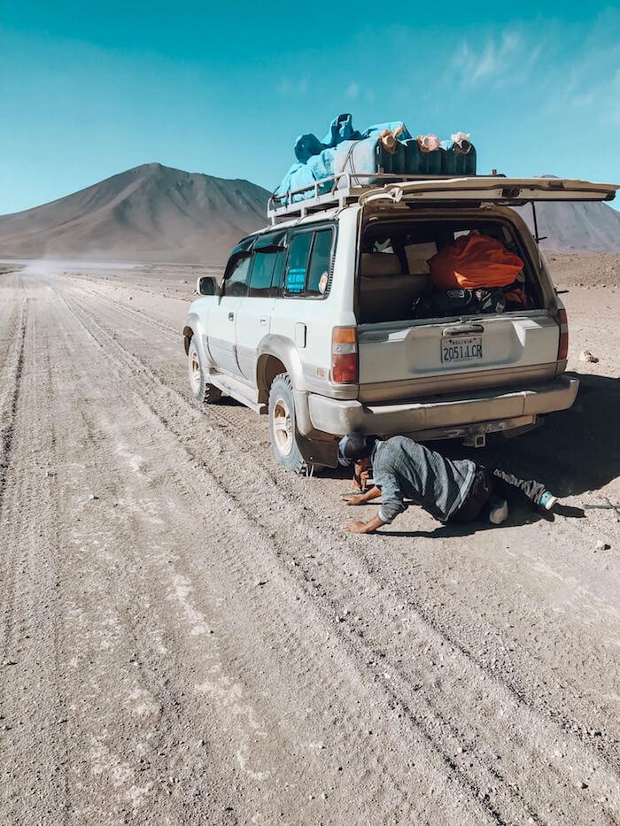 Salar de Uyuni tour - flat tire on the jeep, man on ground fixing tire