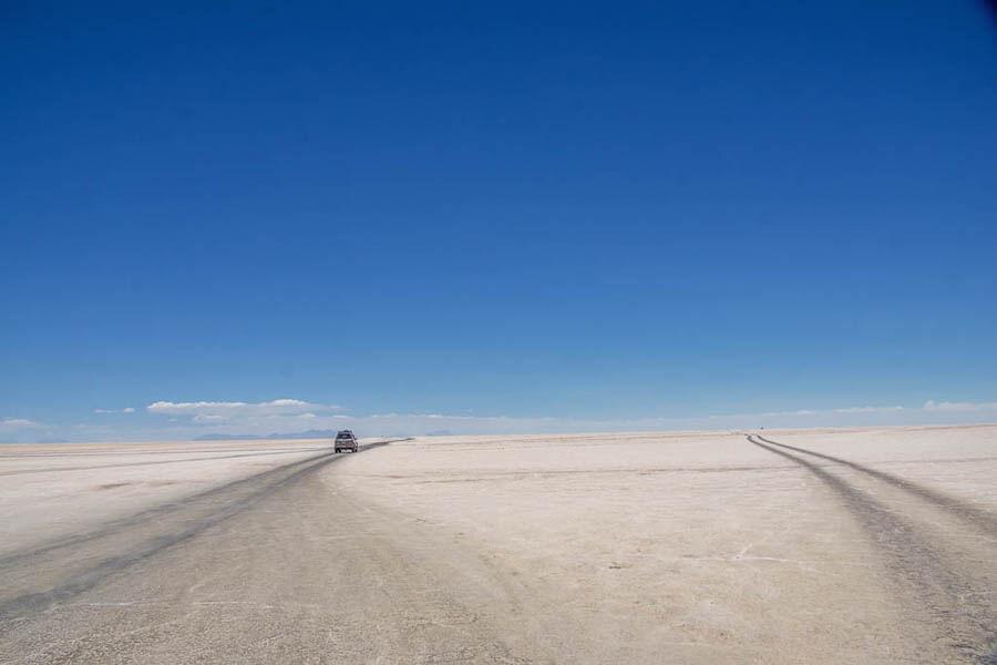 The Salar de uyuni tour | big open white landscape, 2 sets of tire tracks leading to the horizon; one jeep