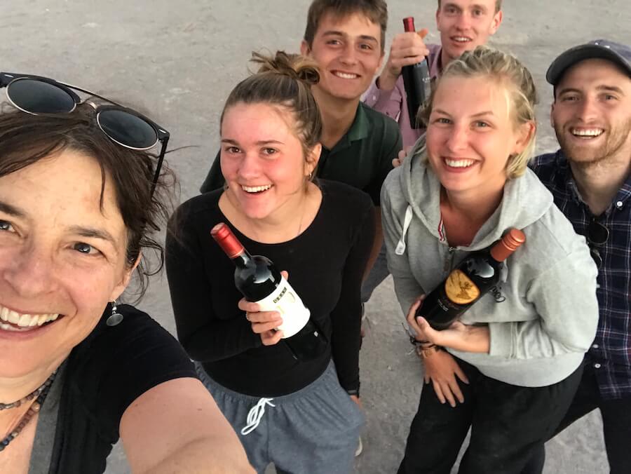 lady taking selfie with group of 5 young people (3 guys,2 girls) holding 2 bottle of wine
