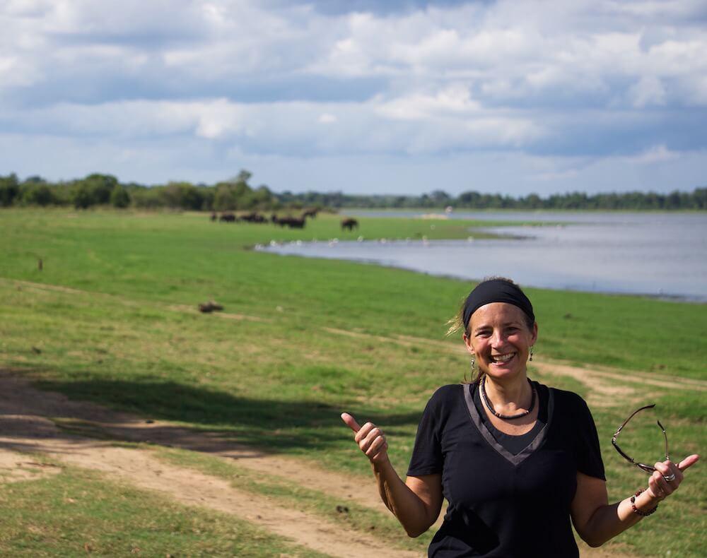 Solo travel as a woman: Minnerya National Park. Solo female traveller smiling with elephants in the distance