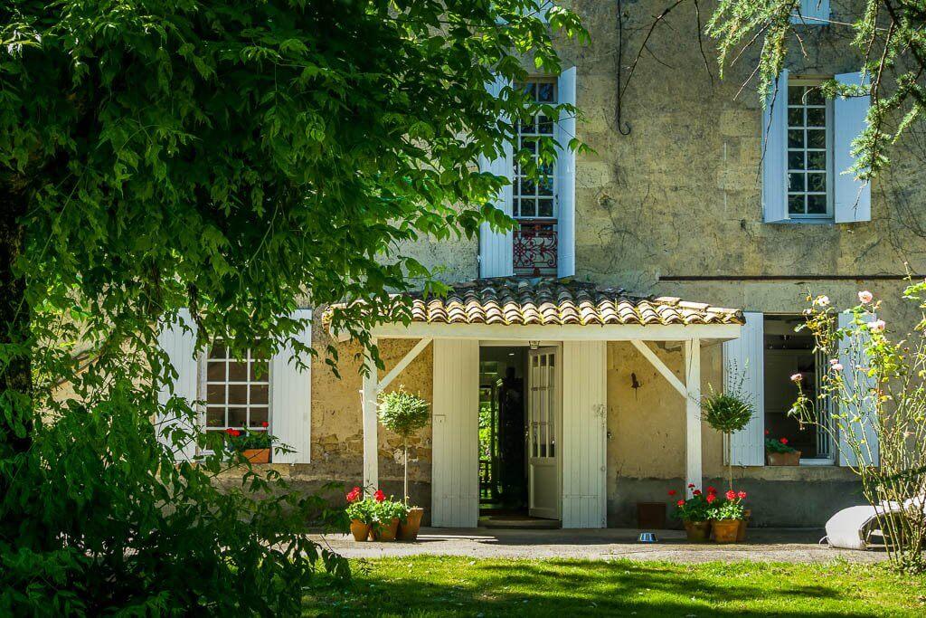 Housesitting: Beautiful house with white shutters and trees in front, red geraniums by door