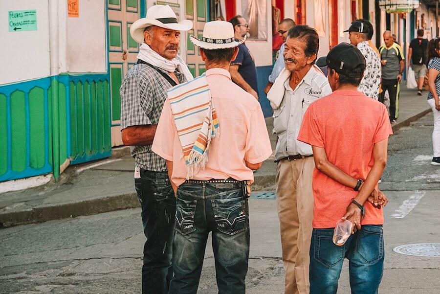 4 men chatting on a street corner - 2 in sombreros and ponchos over the shoulder