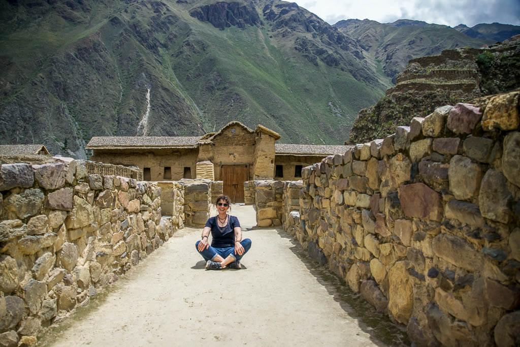 Solo travel as a woman: Woman sitting cross legged between an ancient stone wall. Andes in the background
