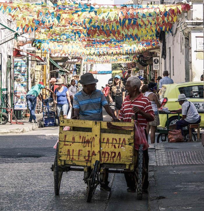 2 Colombian men chatting over a yellow wooden cart with red writing