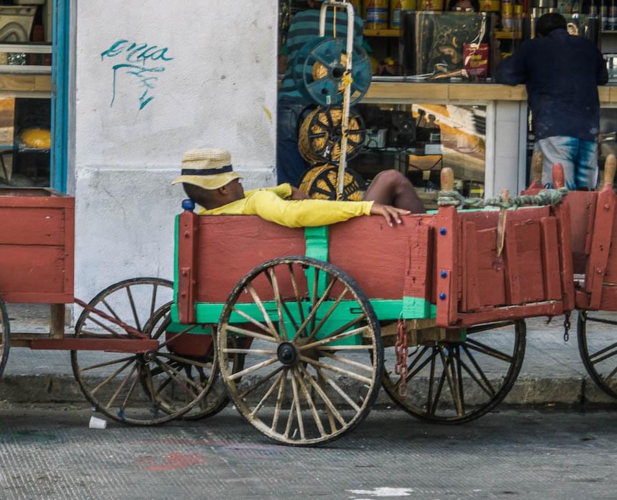 Man in yellow shirt and sombrero sleeping in red cart