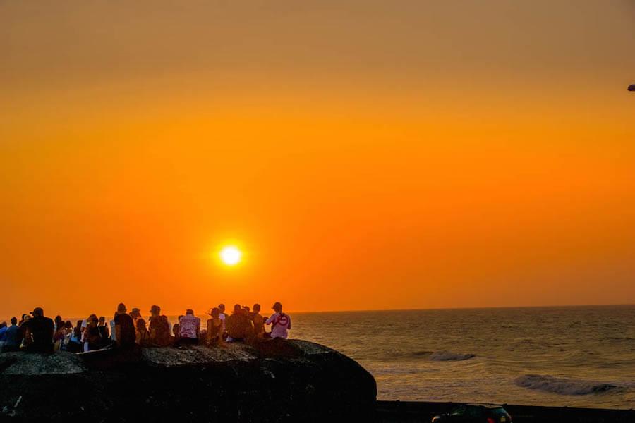 Sun setting over the sea; silhouettes of people on the fortified wall