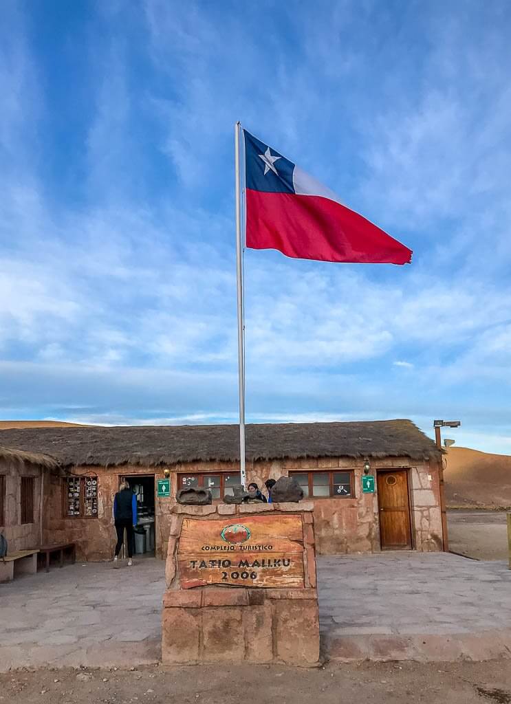 The red, white and blue (with a white star on the blue) flag flaps. Blue sky with wispy clouds at El Tatio
