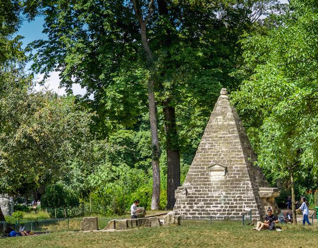 Unique places in Paris: brick pyramid amidst trees. 2 people sitting and reading nearby