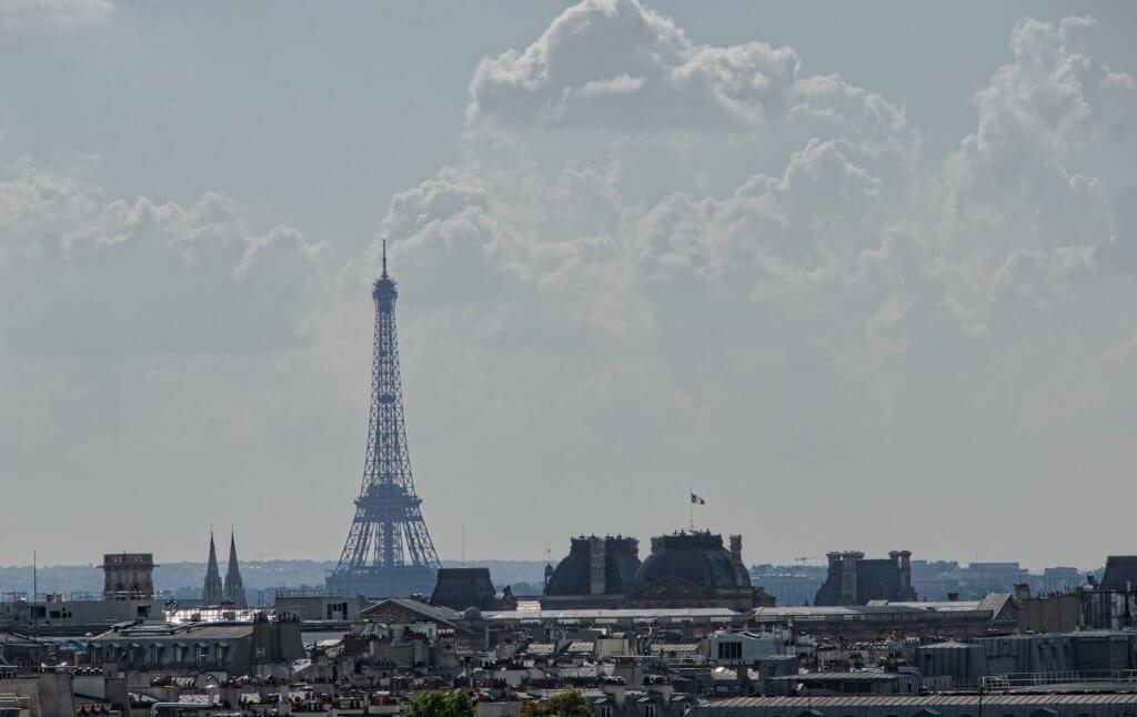 Hidden Gems of Paris| view of the Eiffel tower soaring above rooftops, puffy clouds in sky