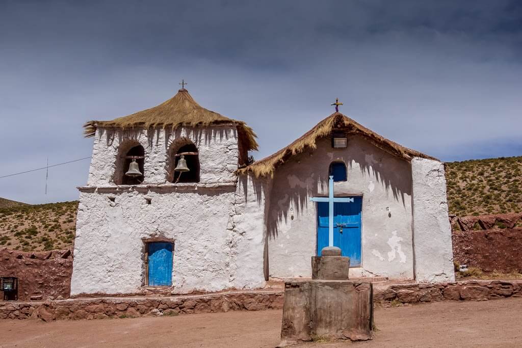 The town of Machupa near El Tatio Geyser Field: whitewashed church with blue doors and cross, thatched roof and 2 bells 