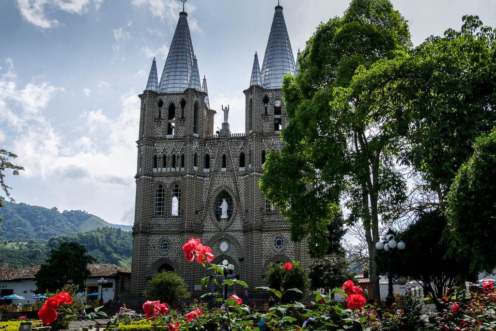 red flowers in foreground and trees, church with 2 towers rising behind