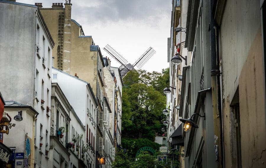 Hidden gems in Paris - windmill peeking overtop trees at the end of a street