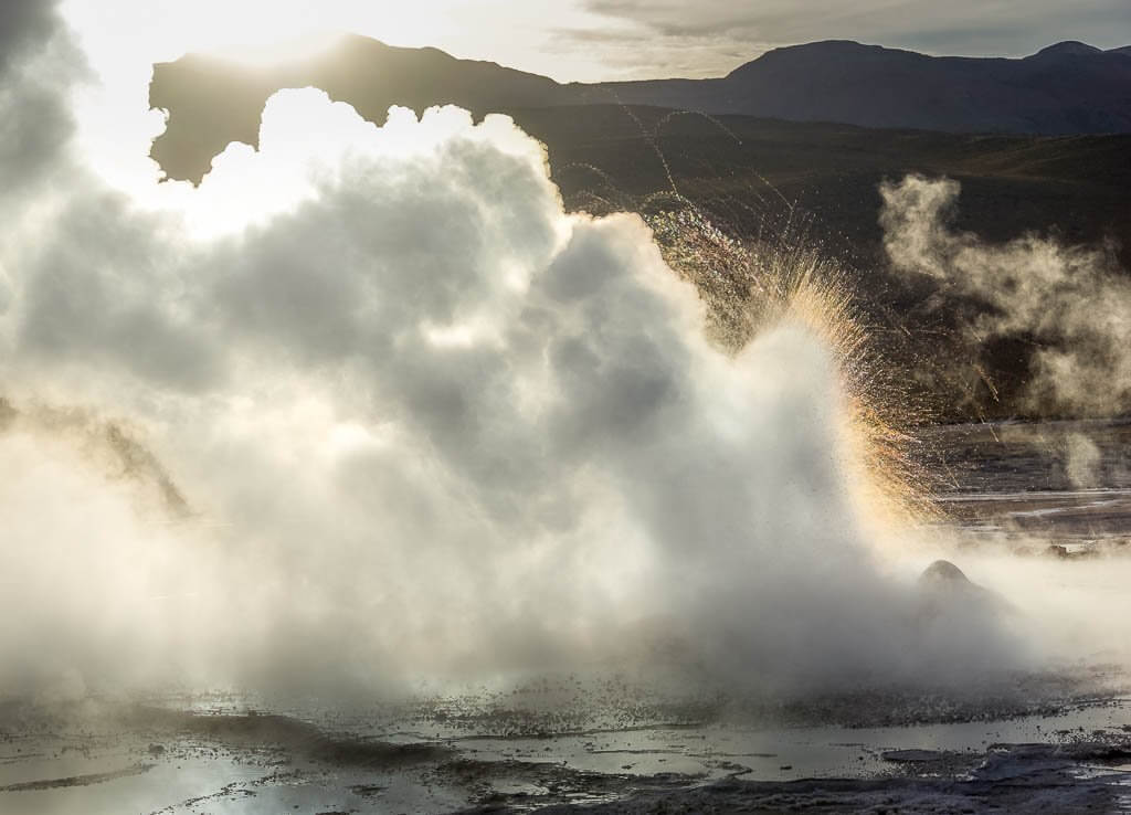 El Tatio Geysers: Billowing Steam and water spraying. Sunrise lighting them from behind 