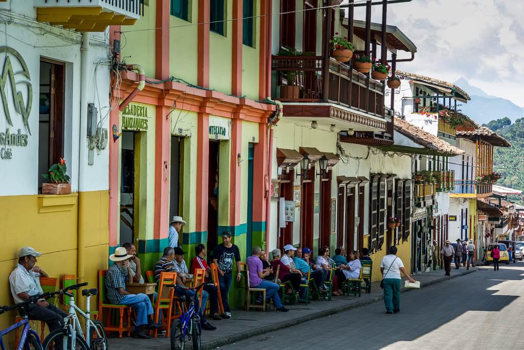people line the street seated on chairs in front of colourful buildings