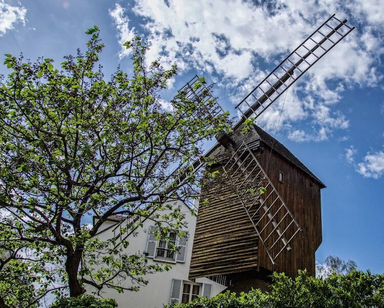 Hidden gems of Paris: wooden windmill with tree in front and blue + cloudy sky behind
