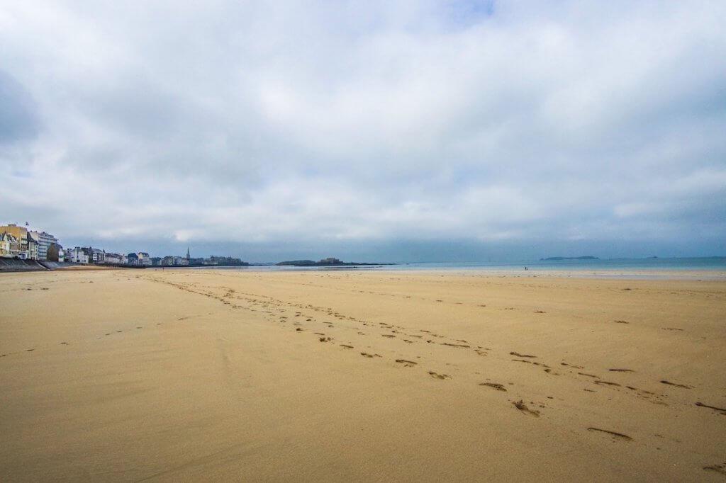 sandy beach with footprints with town in the distance, big cloudy sky: Saint-Malo beach