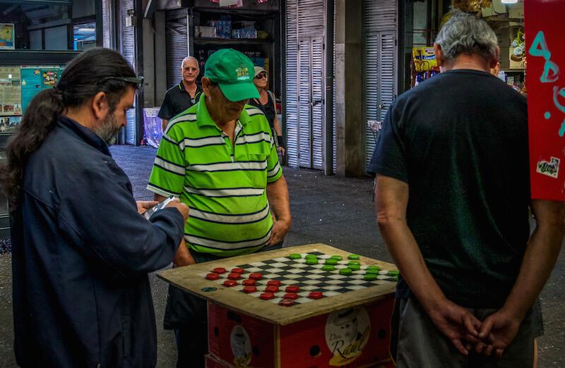 3 men around a checker board - checkers red and lime green; one of the men has a lime green hat and striped shirt that is also lime green