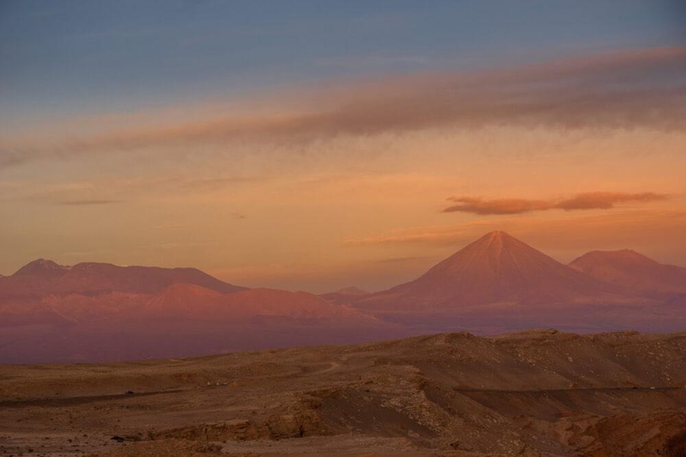 pink and purple hues over the Andes mountains. Rock desert in foreground