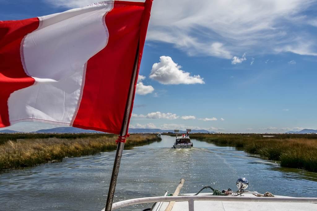 Lake titicaca: the red and white Peruvian flag flutters as the boat heads along a channel 