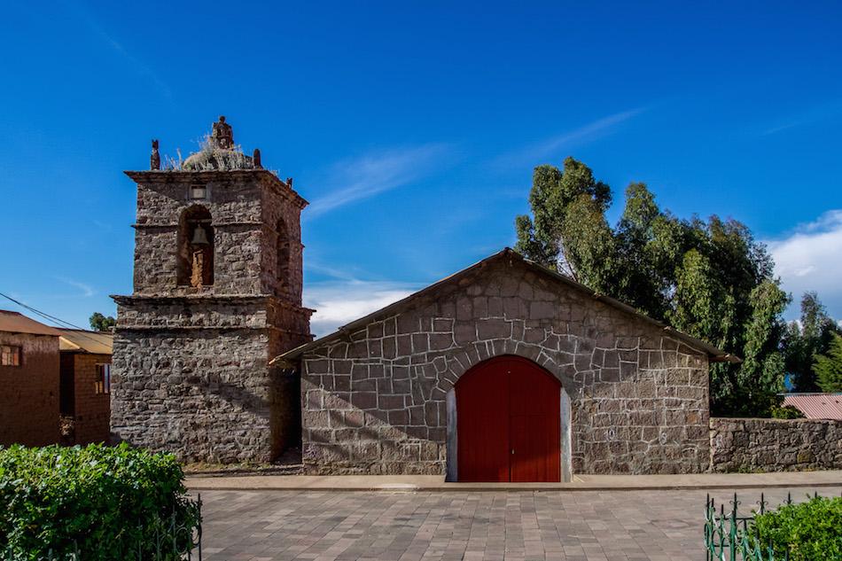 Isla Amantani: the adobe church with a red door, triangular shaped roof and a tower to the left