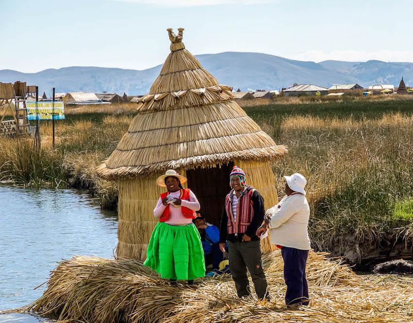 Uros: greeted by 3 people. lady in bright green skirt, reed house behind