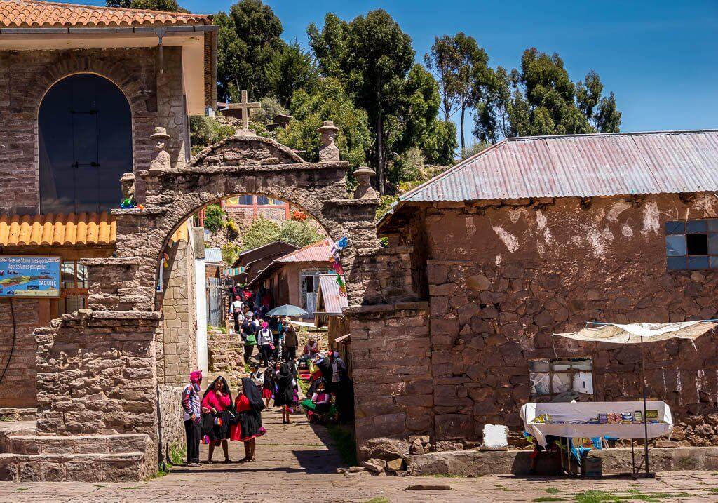 Taquile: adobe buildings and archway with people in traditional dress gathered