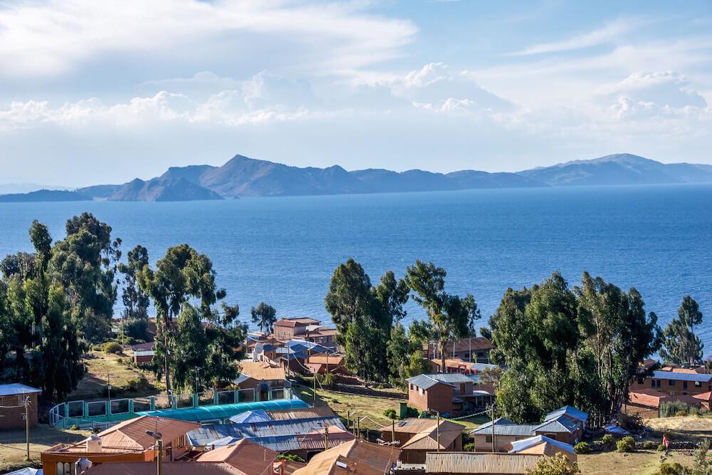 Amantani Island: view over rooftops to the blue waters of the lake titicaca and mountains in the distance