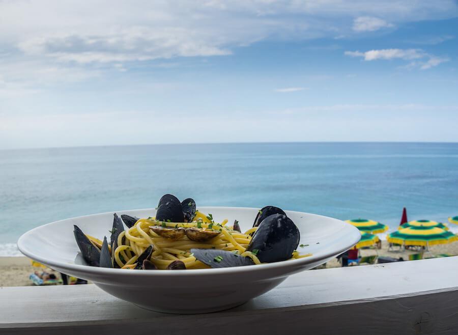 Tropea Calabria- white bowl of spaghetti and mussels with the sea in the background