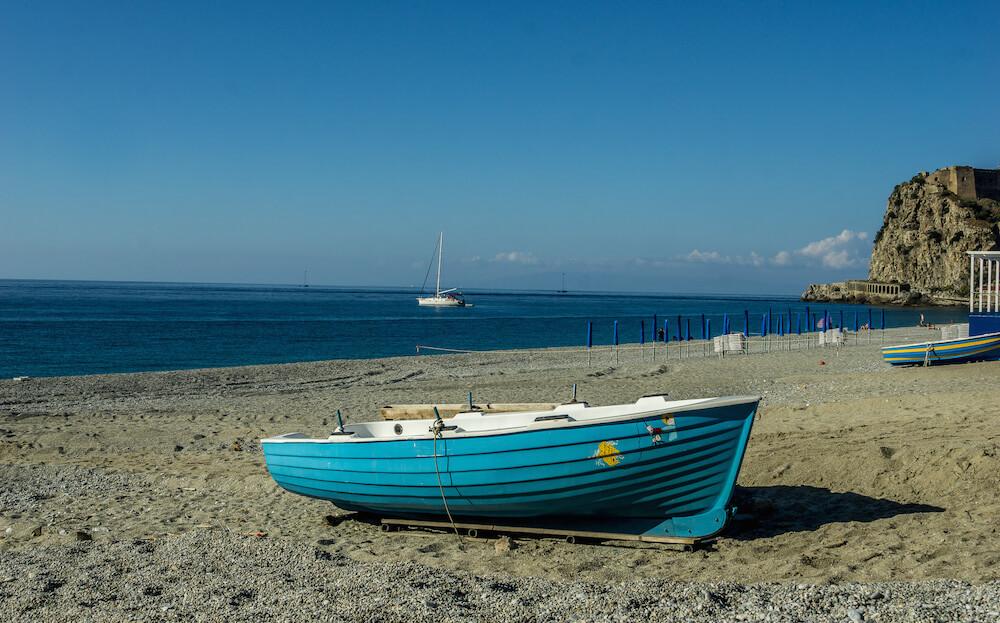 Scilla: a blue fishing boat is pulled on shore with the sea behind