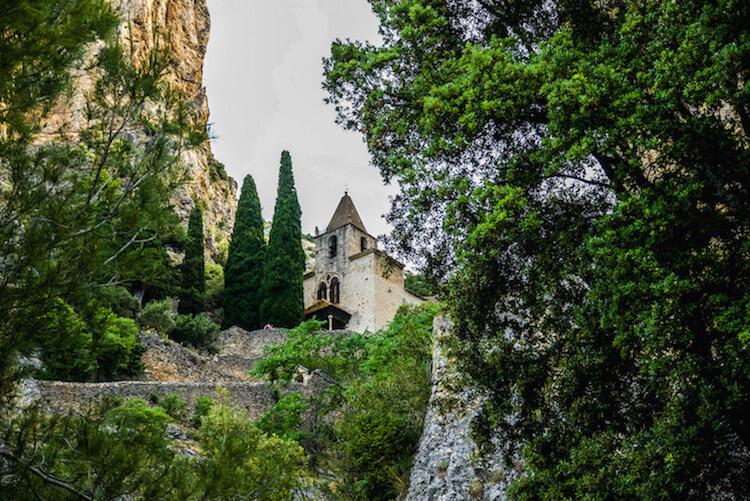 Les Plus Beaux VIllages de France: church nestled on a rock cliff behind 2 cypress trees