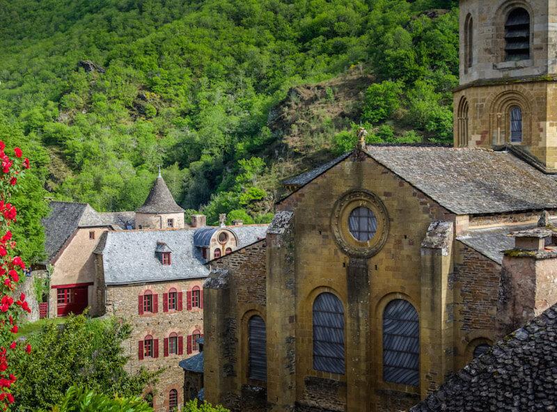 Conques France: part of the church, a building with red shutters framed by red flowers on the left