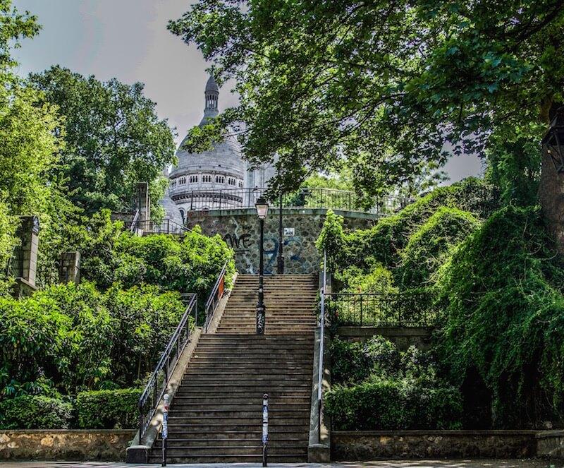 staircase covered by greenery and the white basilica of Sacre Coeur at the top