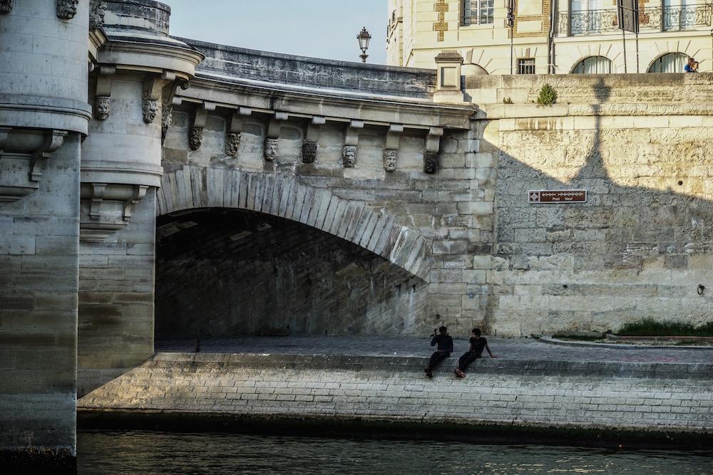 Under Pont Neuf, 2 people are sitting by the Seine